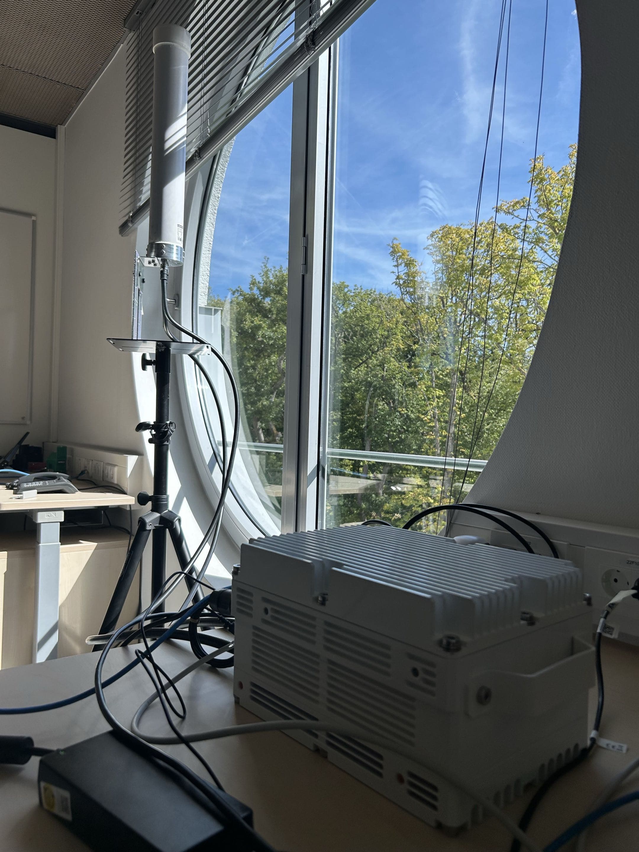 CableFree SC-418 on a lab bench beside a cylindrical omnidirectional antenna with a metal bracket on a black tripod by the window.